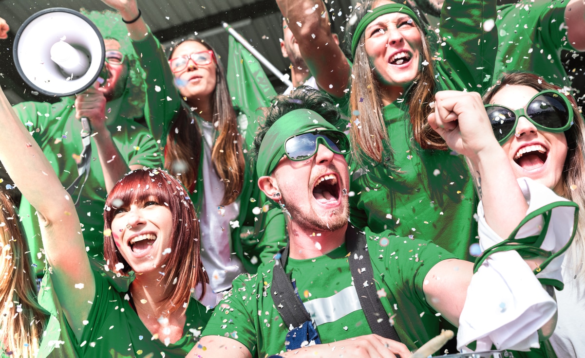 Young amateur football fan supporters cheering with confetti watching local soccer cup match at stadium - Friends people group on green t shirts having excited fun on sport world championship final